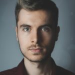 Close-up portrait of a young man with facial hair and a serious expression.